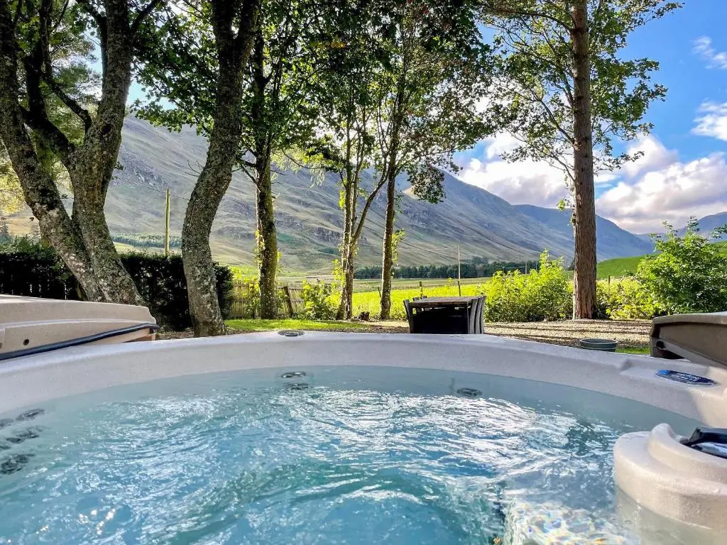 a hot tub in a yard with mountains in the background at Brandy Cottage - Ukc6855 in Millton of Clova