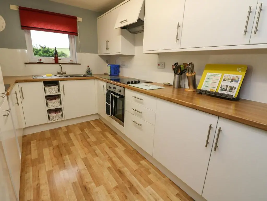 a kitchen with white cabinets and a wooden floor at Bide-a-While in Marnoch