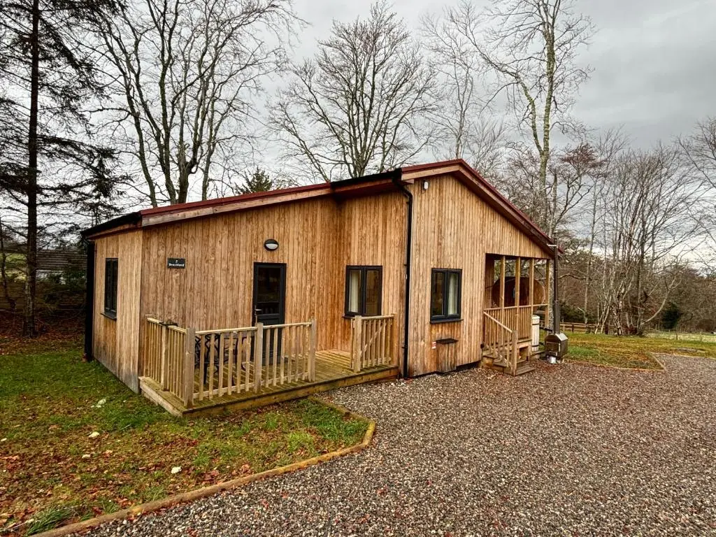 a small wooden building with a porch in a field at Breckland Lodge 2 with Hot Tub in Belladrum