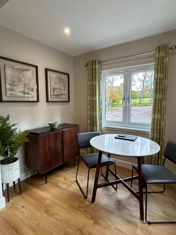 a living room with a table and chairs and a window at Breckland Lodge 2 with Hot Tub in Belladrum