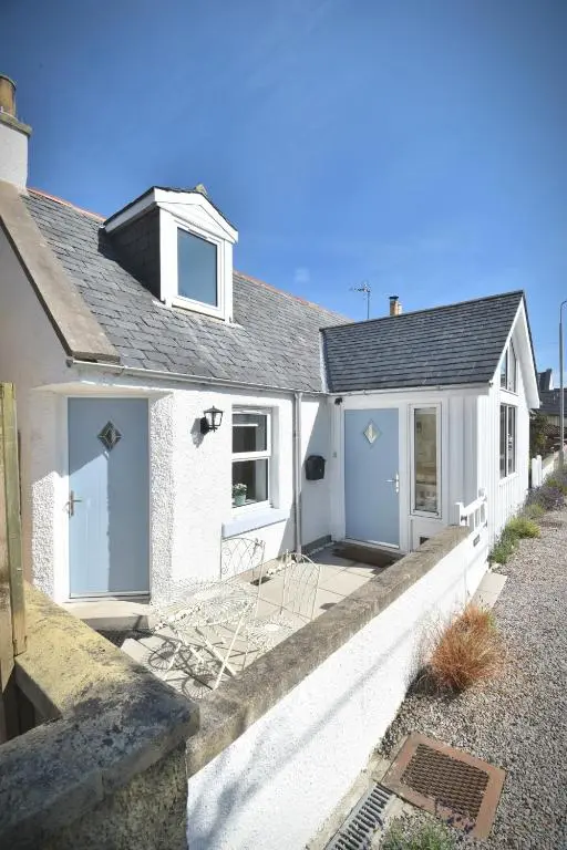 a white house with blue doors on a street at Dram Cottage, Findhorn Bay in Forres
