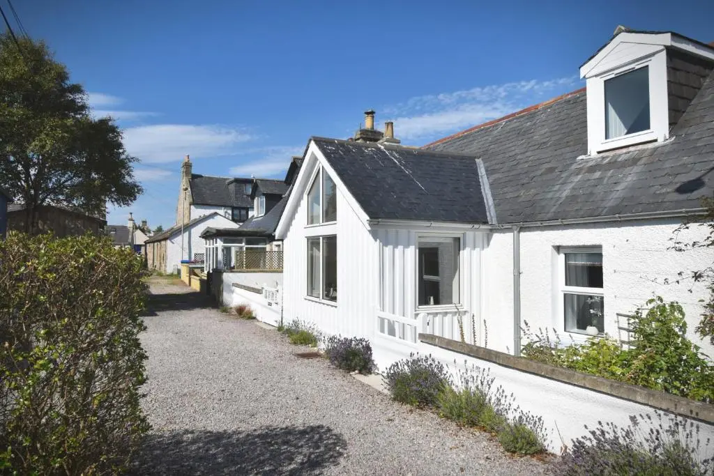 a white house with a black roof on a street at Dram Cottage, Findhorn Bay in Forres