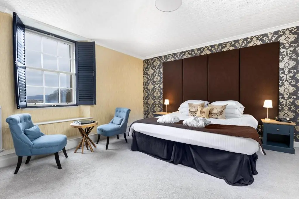 a bedroom with a large bed and two blue chairs at Dornoch Castle Hotel in Dornoch