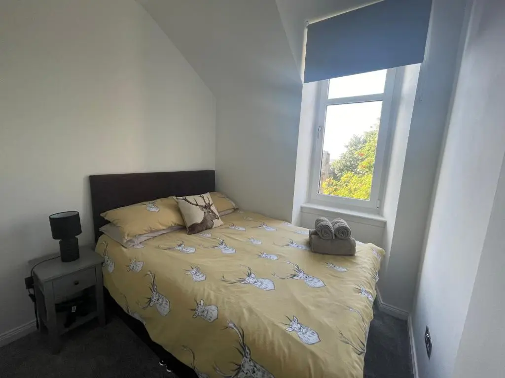 a bedroom with a bed with a yellow comforter and a window at Crown \u00e0ros beag, Ultra City Central 2 bedroom apartment with free parking onsite in Inverness
