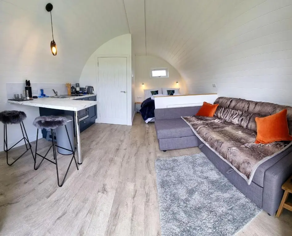 a living room with a couch and a table and a kitchen at Bombie Glamping Pod in Grantown on Spey