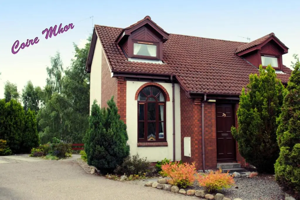 a brown and white house with trees and bushes at Cairngorm Highland Bungalows in Aviemore