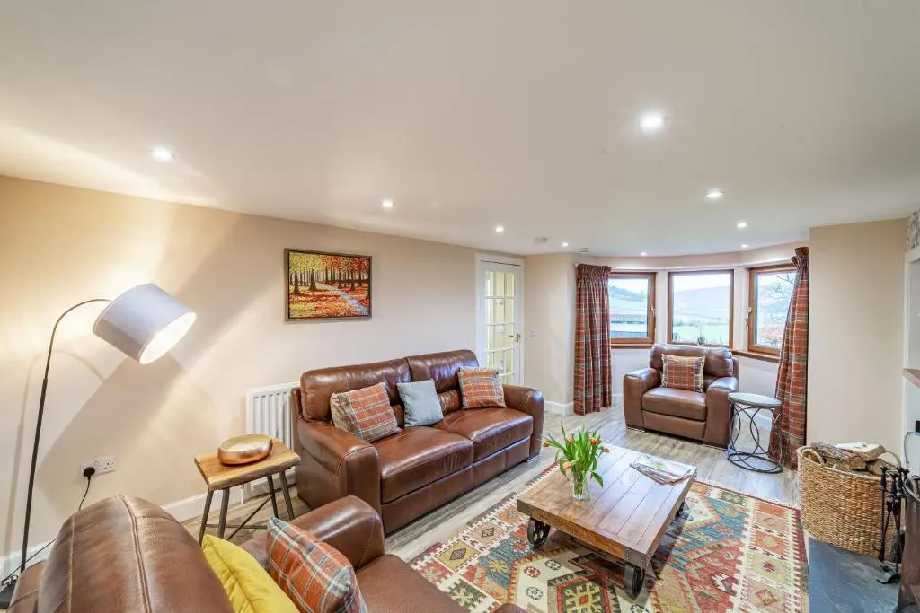 a living room with leather furniture and a table at Gardener\u2019s Cottage with Hot Tub in Blairgowrie