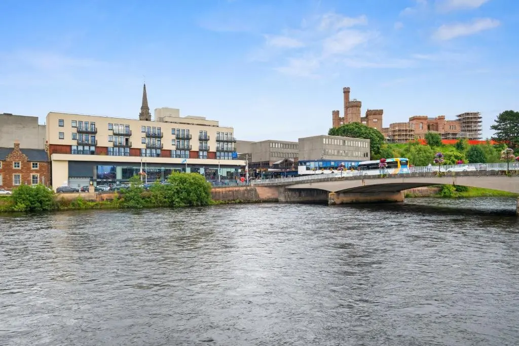 a bridge over a river in a city with buildings at By the Bridge by Toppo in Inverness