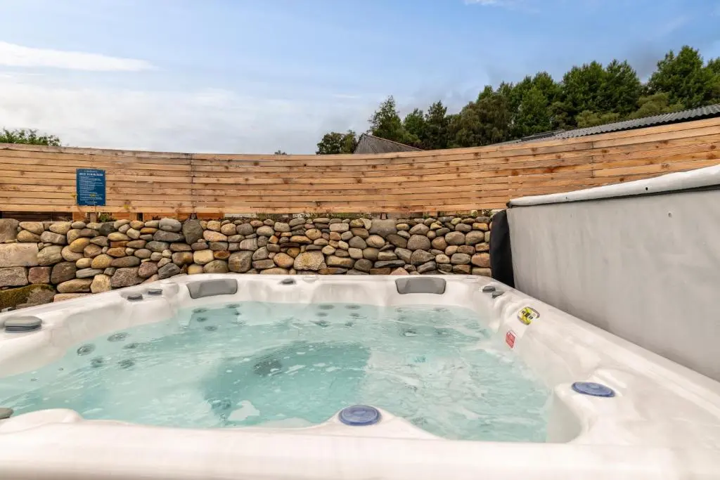 a hot tub in a backyard with a stone wall at Ailsa- Enchanting Tiny House with wood burner and hot tub in Cairngorms in Ballater