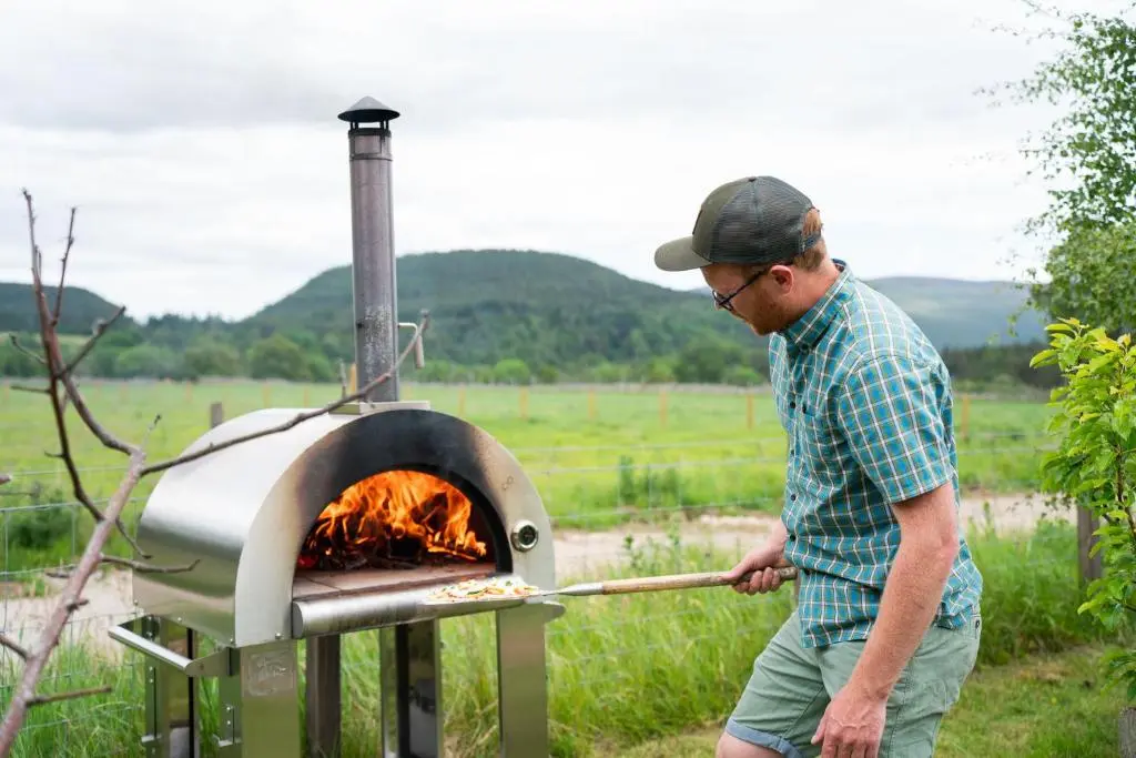 a man is cooking food in an oven at Ailsa- Enchanting Tiny House with wood burner and hot tub in Cairngorms in Ballater