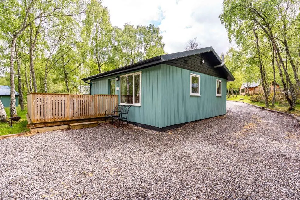 a green tiny house on a gravel driveway at Bracken Lodge 15 with Hot Tub in Belladrum