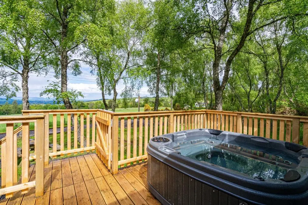 a hot tub on a wooden deck with trees at Bracken Lodge 15 with Hot Tub in Belladrum