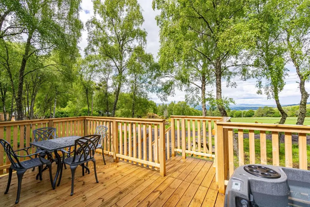 a patio with a table and chairs on a wooden deck at Bracken Lodge 15 with Hot Tub in Belladrum