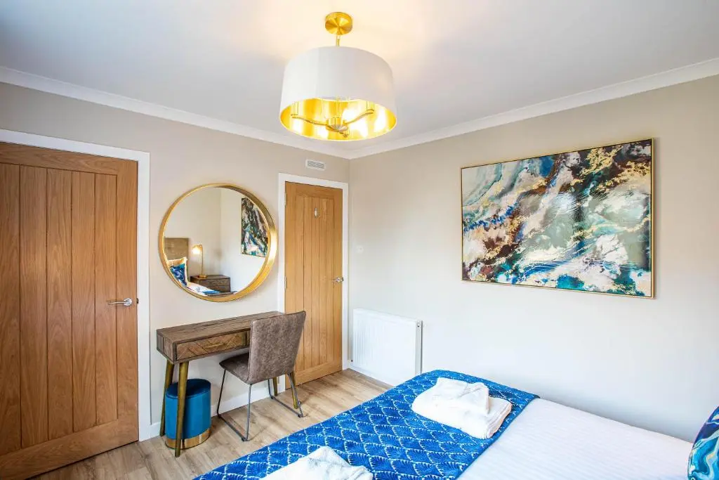 a bedroom with a bed and a desk and a mirror at Breckland House with Hot Tub in Belladrum