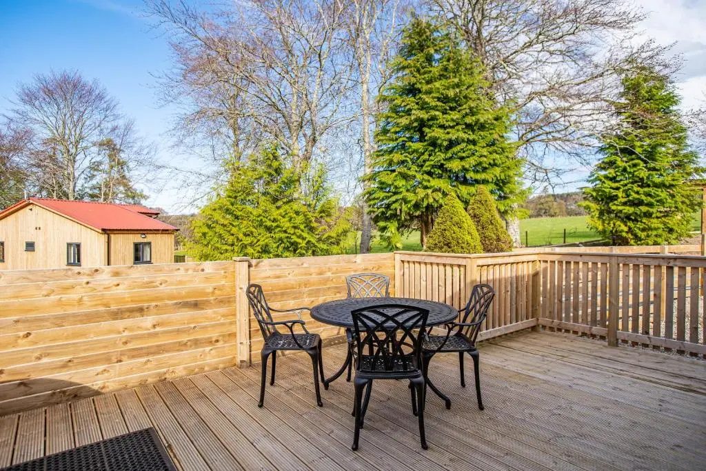a patio with a table and chairs on a wooden deck at Breckland House with Hot Tub in Belladrum