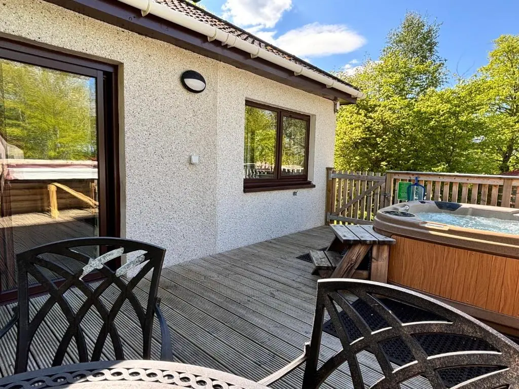 a wooden deck with two chairs and a hot tub at Breckland House with Hot Tub in Belladrum