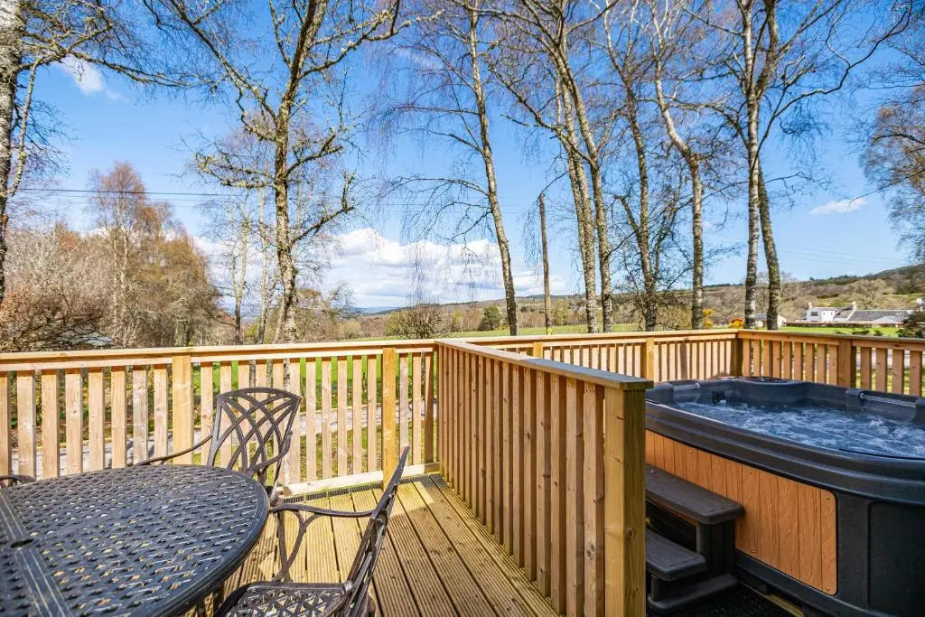 a table and chairs on a deck with a hot tub at Heather Lodge 1 with Hot Tub in Belladrum