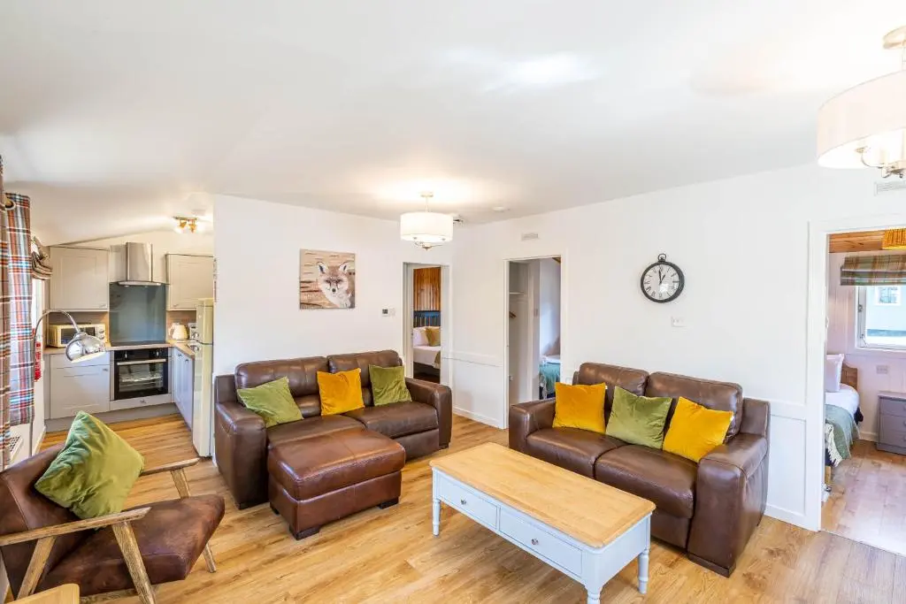 a living room with brown leather furniture and yellow pillows at Heather Lodge 1 with Hot Tub in Belladrum