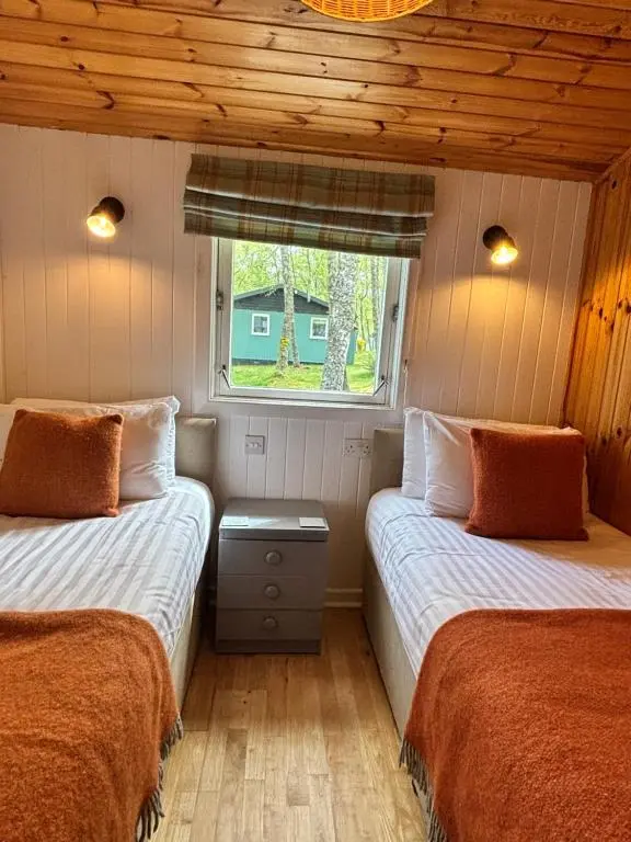 two beds in a small room with a window at Heather Lodge 1 with Hot Tub in Belladrum