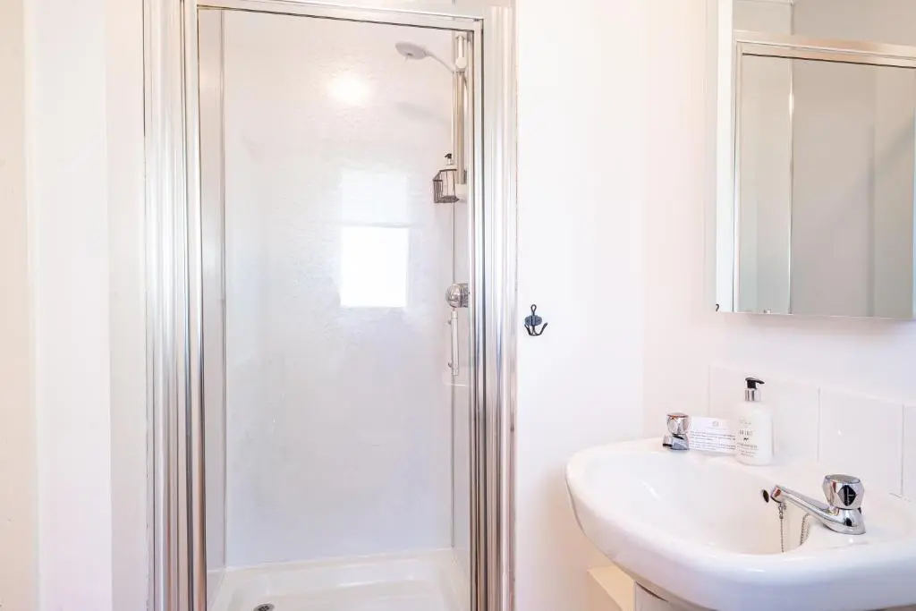 a white bathroom with a shower and a sink at Heather Lodge 3 with Hot Tub in Belladrum