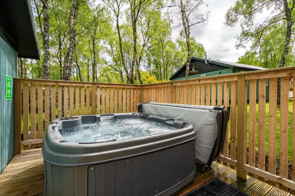 a hot tub on a deck with a fence at Heather Lodge 3 with Hot Tub in Belladrum