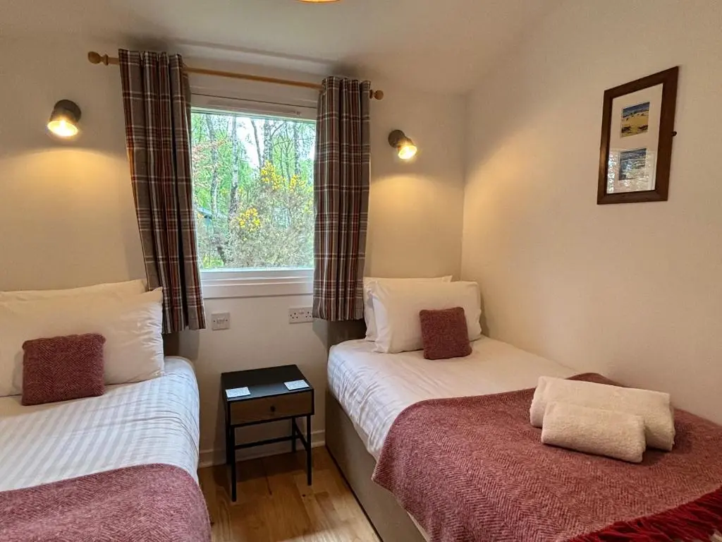 two beds in a small room with a window at Heather Lodge 3 with Hot Tub in Belladrum