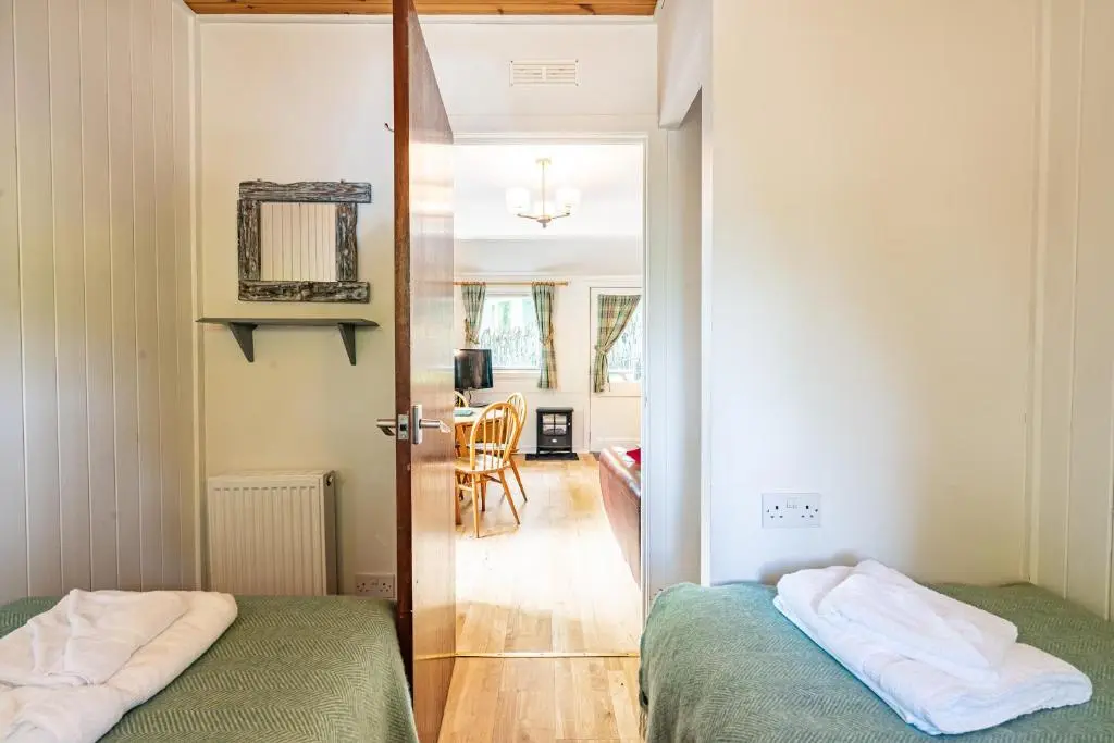 a bedroom with two beds and a door leading to a kitchen at Heather Lodge 10 with Hot Tub in Belladrum