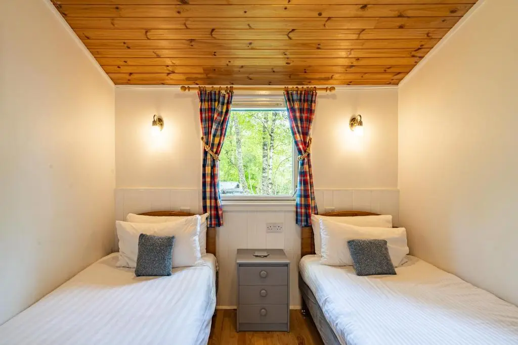 two twin beds in a room with a window at Heather Lodge 10 with Hot Tub in Belladrum