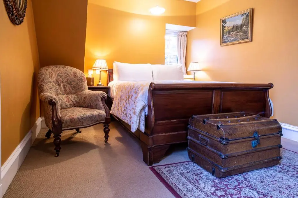 a bedroom with a bed with a chair and a chair at Dalmunzie Castle Hotel in Glenshee