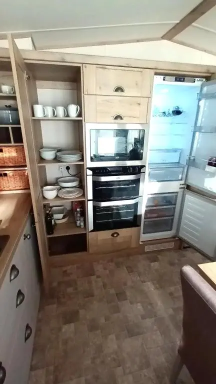 a kitchen with wooden cabinets and an open refrigerator at Binka - Luxury 40 x 14ft Lodge in Tain