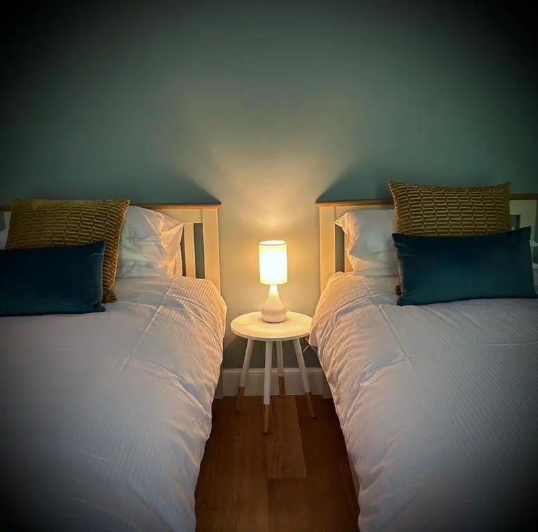 two beds in a room with a lamp on a table at The Fiddich Luxury Home in Craigellachie in Craigellachie