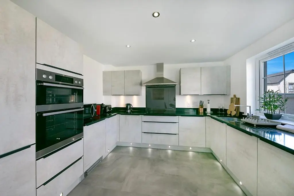 a large kitchen with white cabinets and black appliances at Fern Place Villa - Grampian Lettings Ltd in West Cults