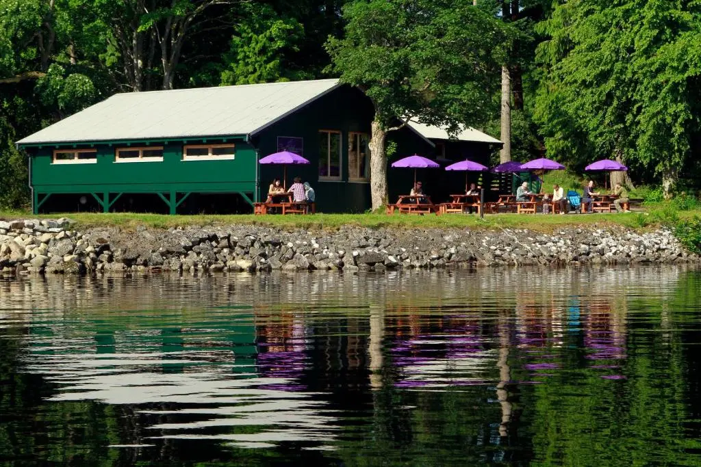 a building with tables and purple umbrellas near a body of water at The Highland Club in Fort Augustus