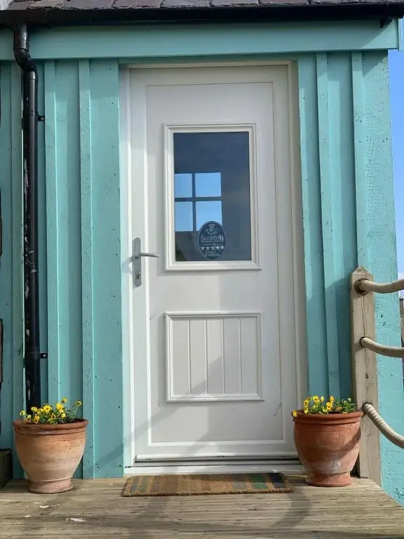 a white door on a blue building with two pots at The Millie Luxury Five Star with Sea View in Burghead