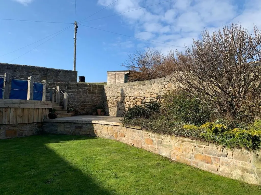 a stone retaining wall with a grass yard and a building at The Millie Luxury Five Star with Sea View in Burghead
