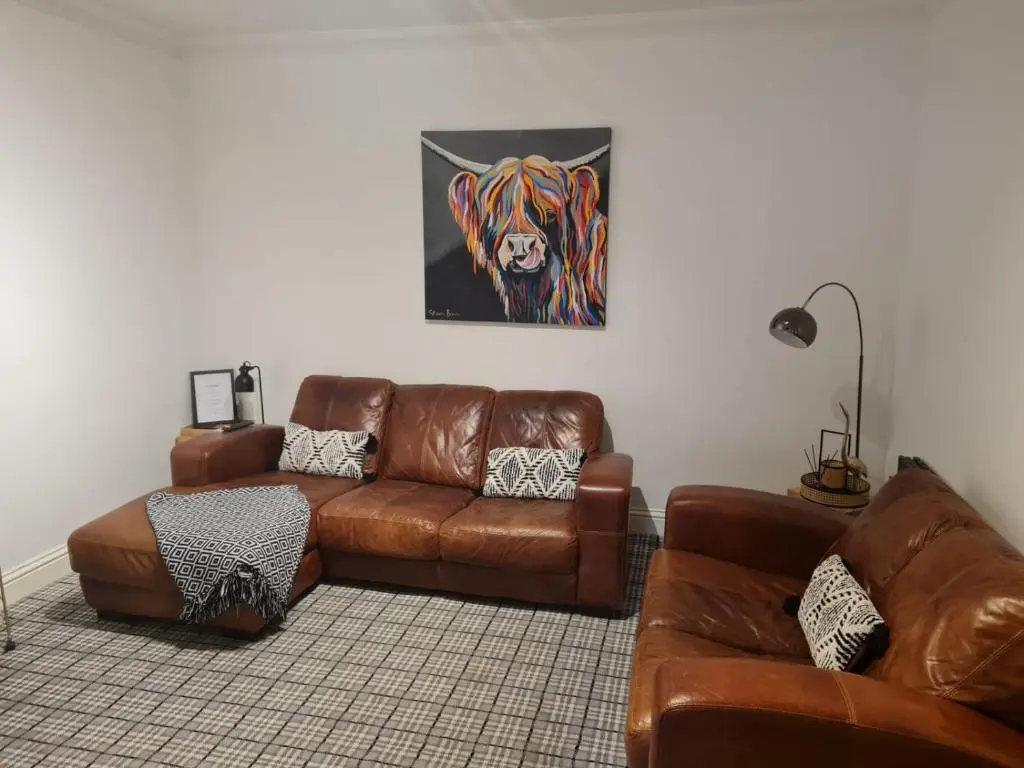 a living room with a leather couch and a lion painting at Cullen Holiday Home in Cullen