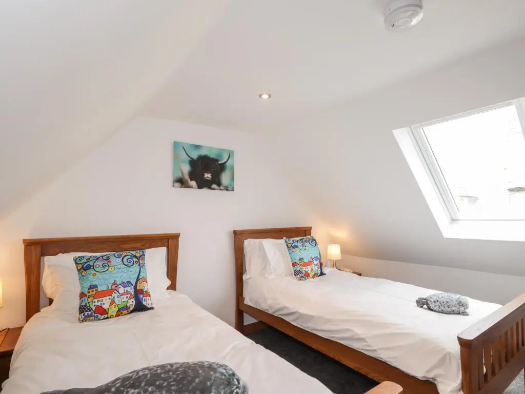 two beds in a room with two windows at Corner Cottage in Buckie