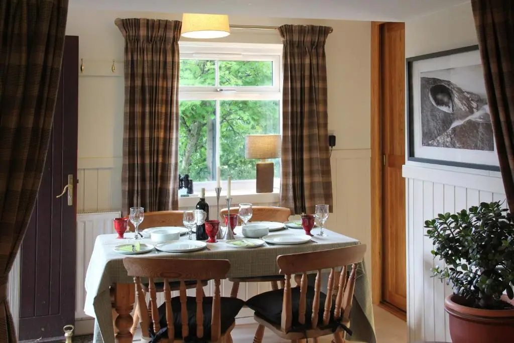 a dining room table with chairs and a window at Smithy Cottage in Strathdon