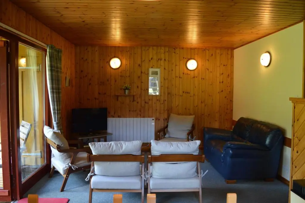 a living room with a table and chairs and a tv at Reuben's Highland Retreat - Speyside in Carrbridge