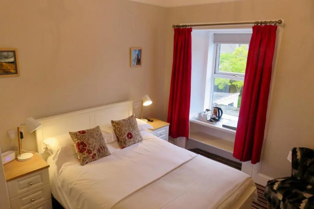 a bedroom with a bed with red curtains and a window at West End Guest House in Elgin