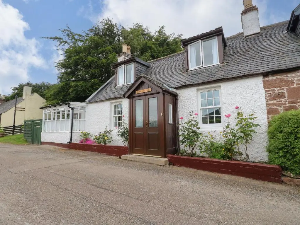 a white house with a brown door on a street at Rose Cottage in Strathpeffer