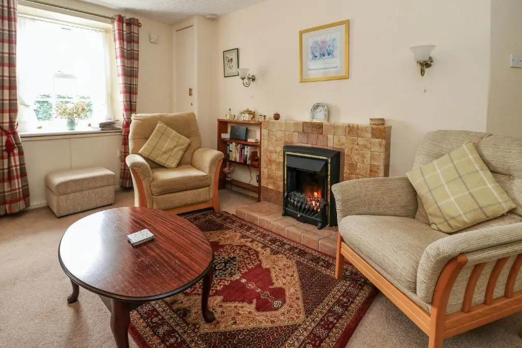 a living room with a fireplace and a couch and a table at Rose Cottage in Strathpeffer