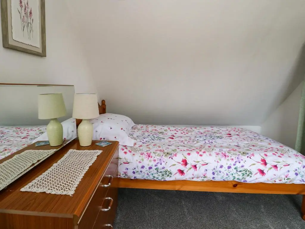 a bedroom with two beds and a desk with two lamps at Rose Cottage in Strathpeffer