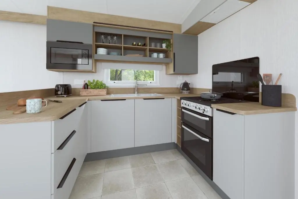 a kitchen with white cabinets and black appliances at The Distiller\u2019s Van - Beautiful, luxury static caravan in Aberlour