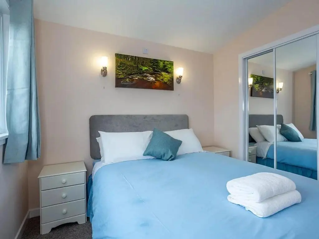 a bedroom with a blue bed and a mirror at Kilninver Chalet on Reelig Estate in Kirkhill