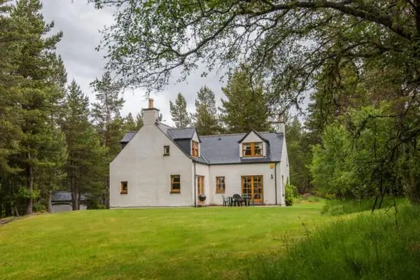 a large white house on a green lawn at Rymore Wood Lodge - Seasgair Lodges in Nethy Bridge