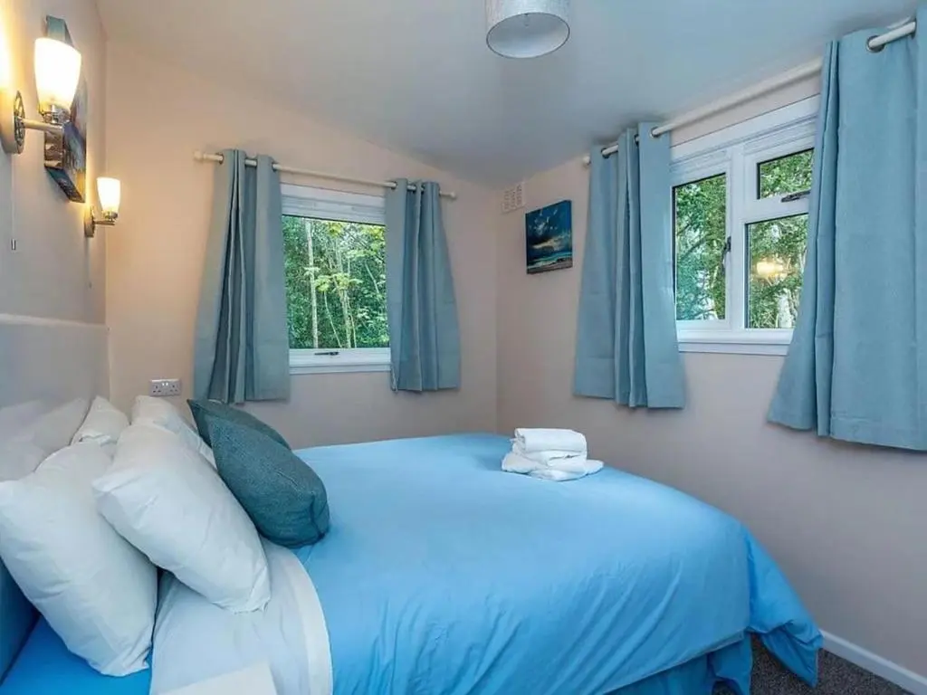 a bedroom with a blue bed and two windows at Bridgend Chalet on Reelig Estate in Kirkhill