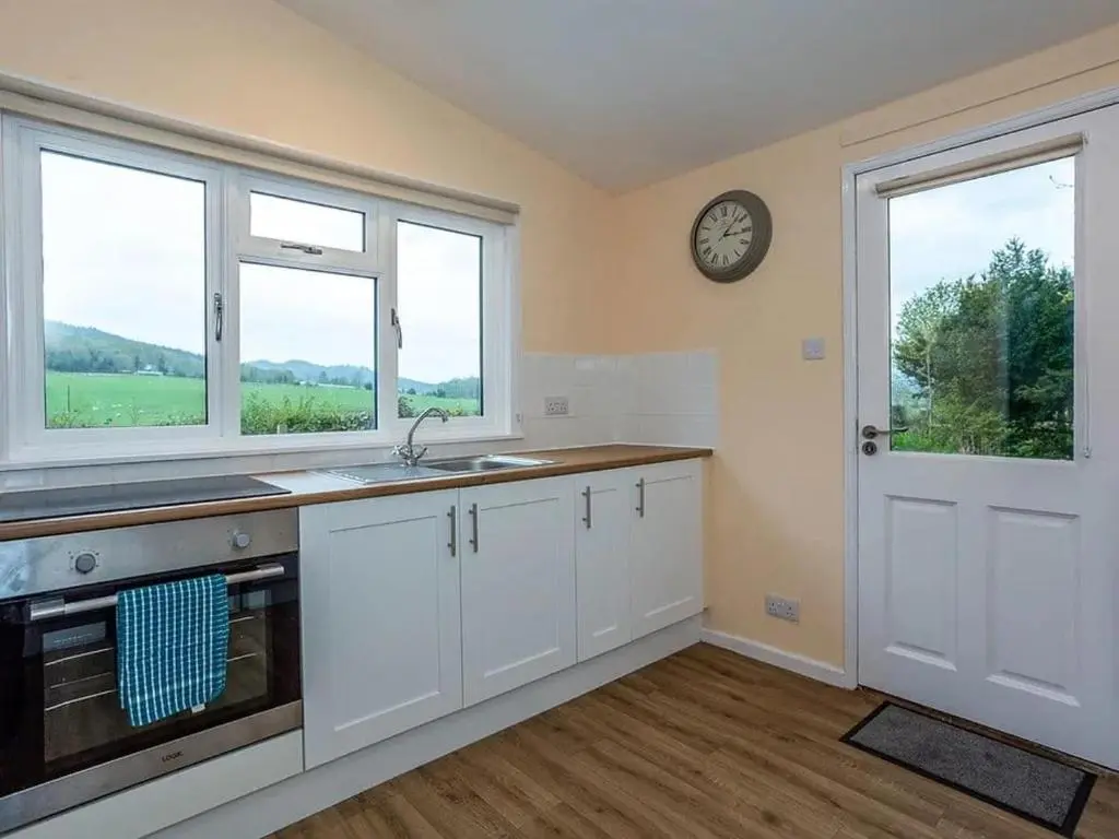 a kitchen with white cabinets and a clock on the wall at Bridgend Chalet on Reelig Estate in Kirkhill