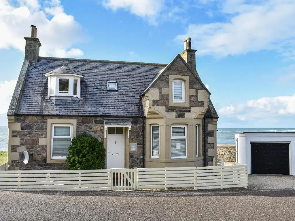 a stone house with a white fence in front of the ocean at Strathlene Lodge in Ianstown