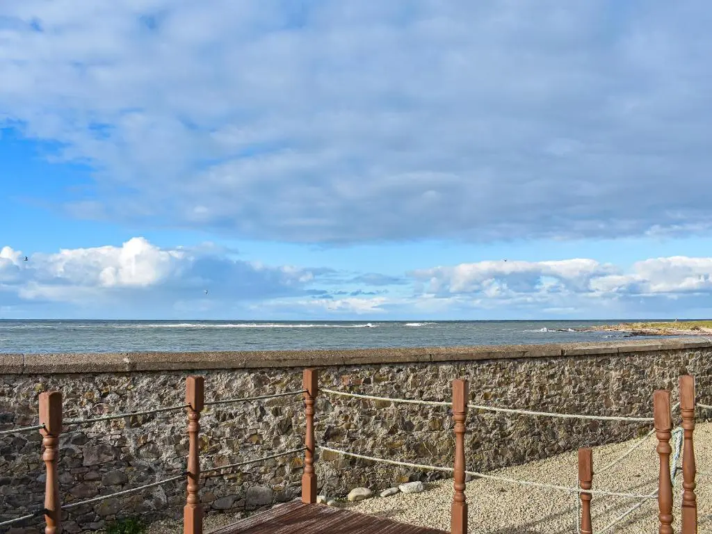a beach with a stone wall and the ocean at Strathlene Lodge in Ianstown